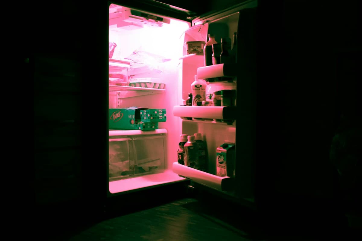 Open refrigerator filled with bottles in a dark kitchen at night