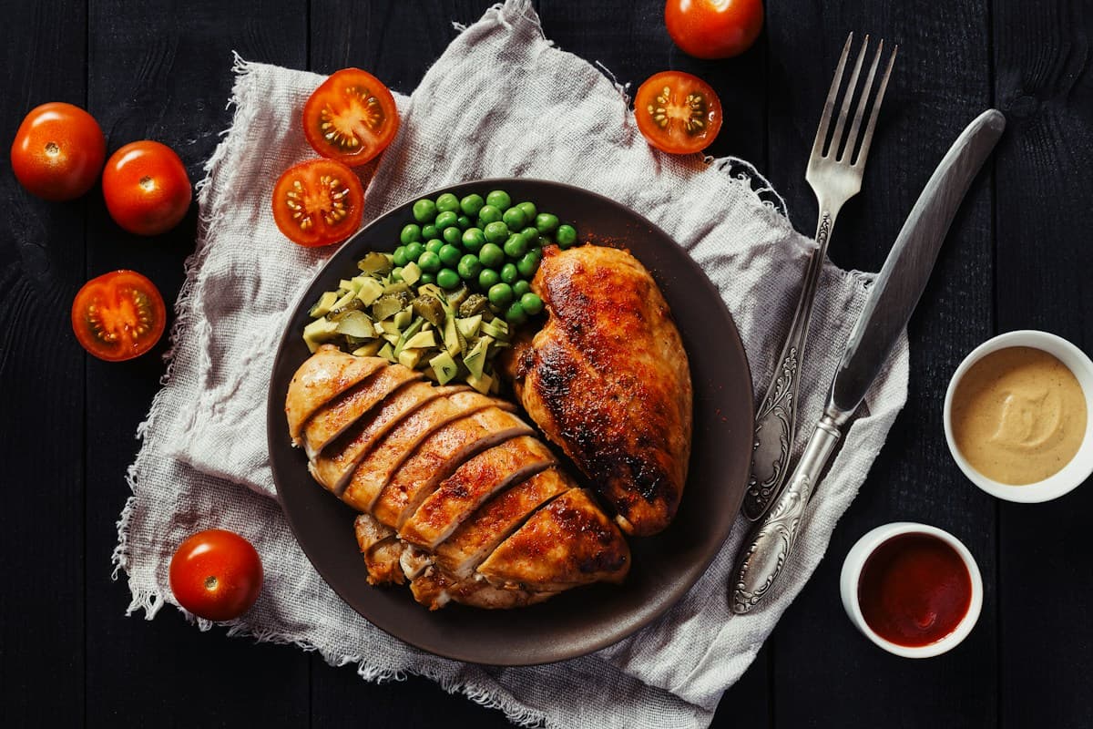 Sliced chicken breast served with green peas on a dark plate