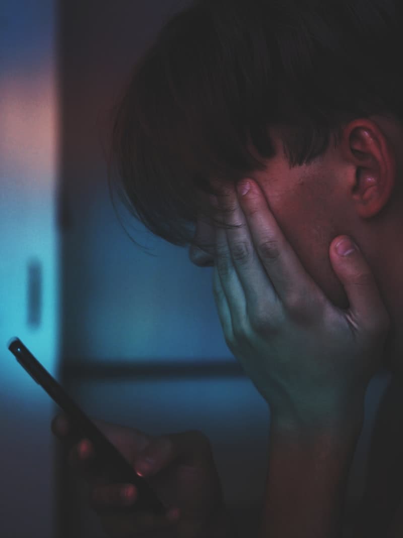 A close-up of a hand holding a smartphone showing a blue chat and comment feed in a dark room