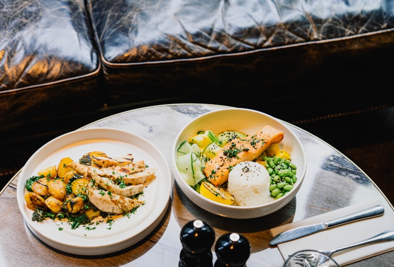 Two healthy meal plates featuring grilled chicken and salmon with fresh vegetables